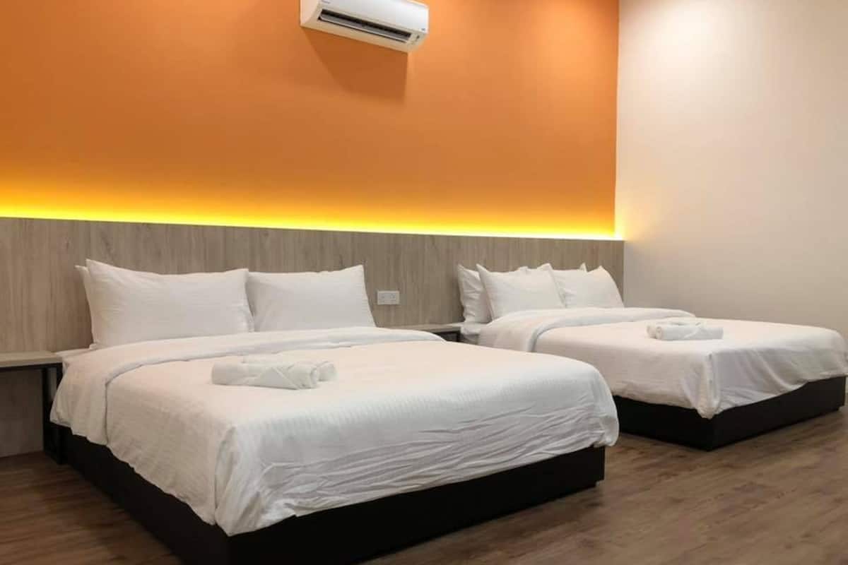 A hotel room with two beds, each with white bedding and pillows, a wooden floor, and an air conditioning unit mounted on the wall.