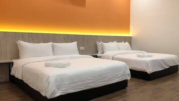 Habitación de hotel con dos camas, cada una con ropa blanca y almohadas, piso de madera y un equipo de aire acondicionado montado en la pared.