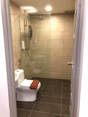 Une salle de bain avec une douche à parois de verre, des toilettes blanches et une serviette posée sur le siège.