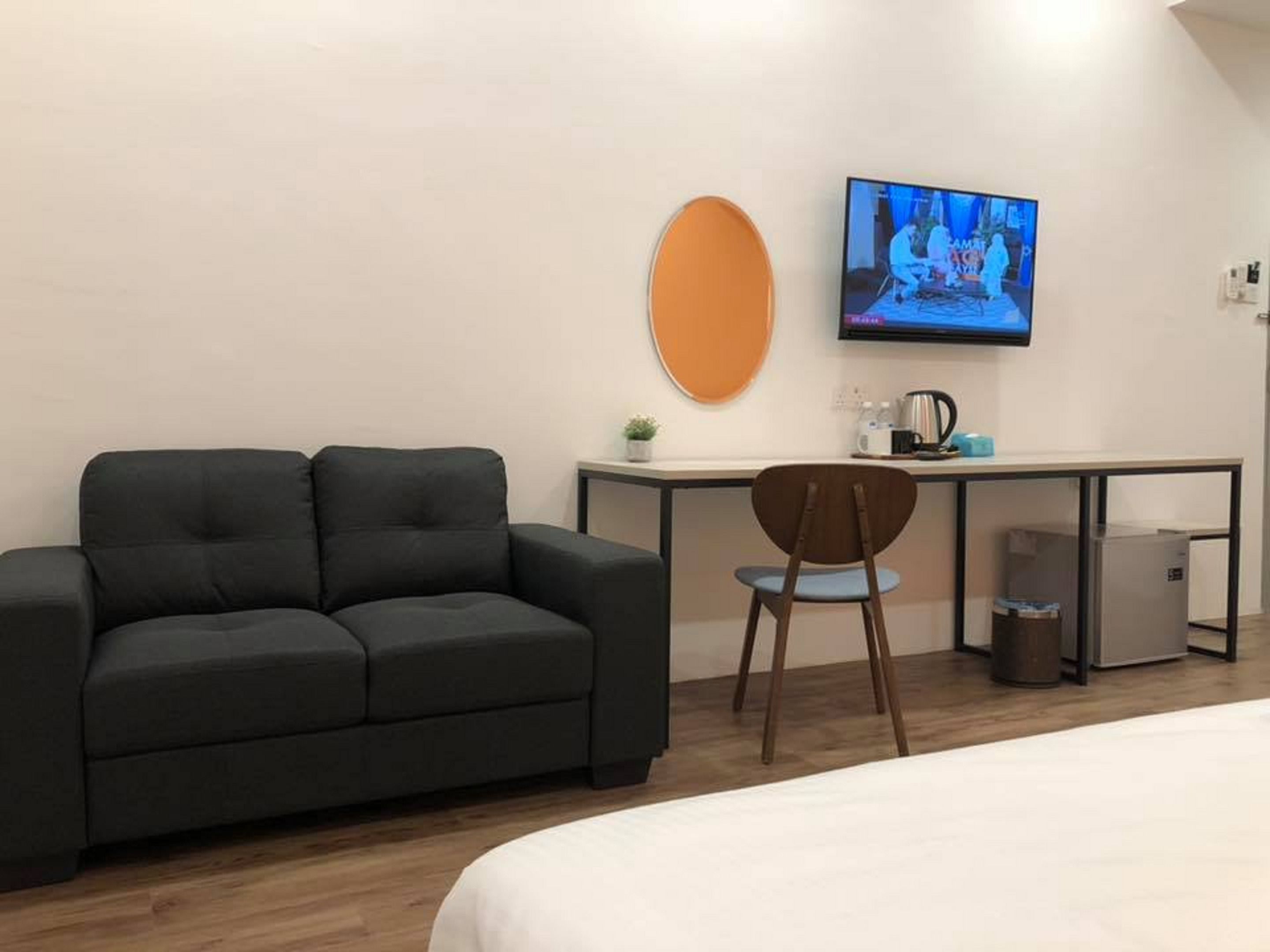 Une chambre d’hôtel moderne avec un canapé gris foncé, une chaise en bois, un petit bureau avec une télévision et un lit.