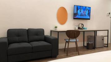 Une chambre d’hôtel moderne avec un canapé gris foncé, une chaise en bois, un petit bureau avec une télévision et un lit.