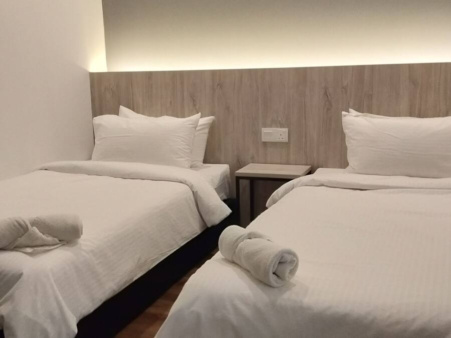 A hotel room with two single beds, each with a neatly folded towel, a wooden headboard, and a small bedside table.