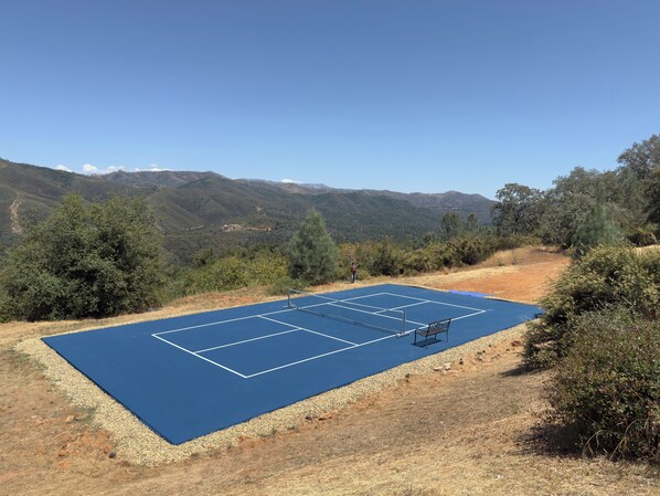 Un court de tennis en plein air offrant une vue dégagée sur les collines et les arbres environnants.