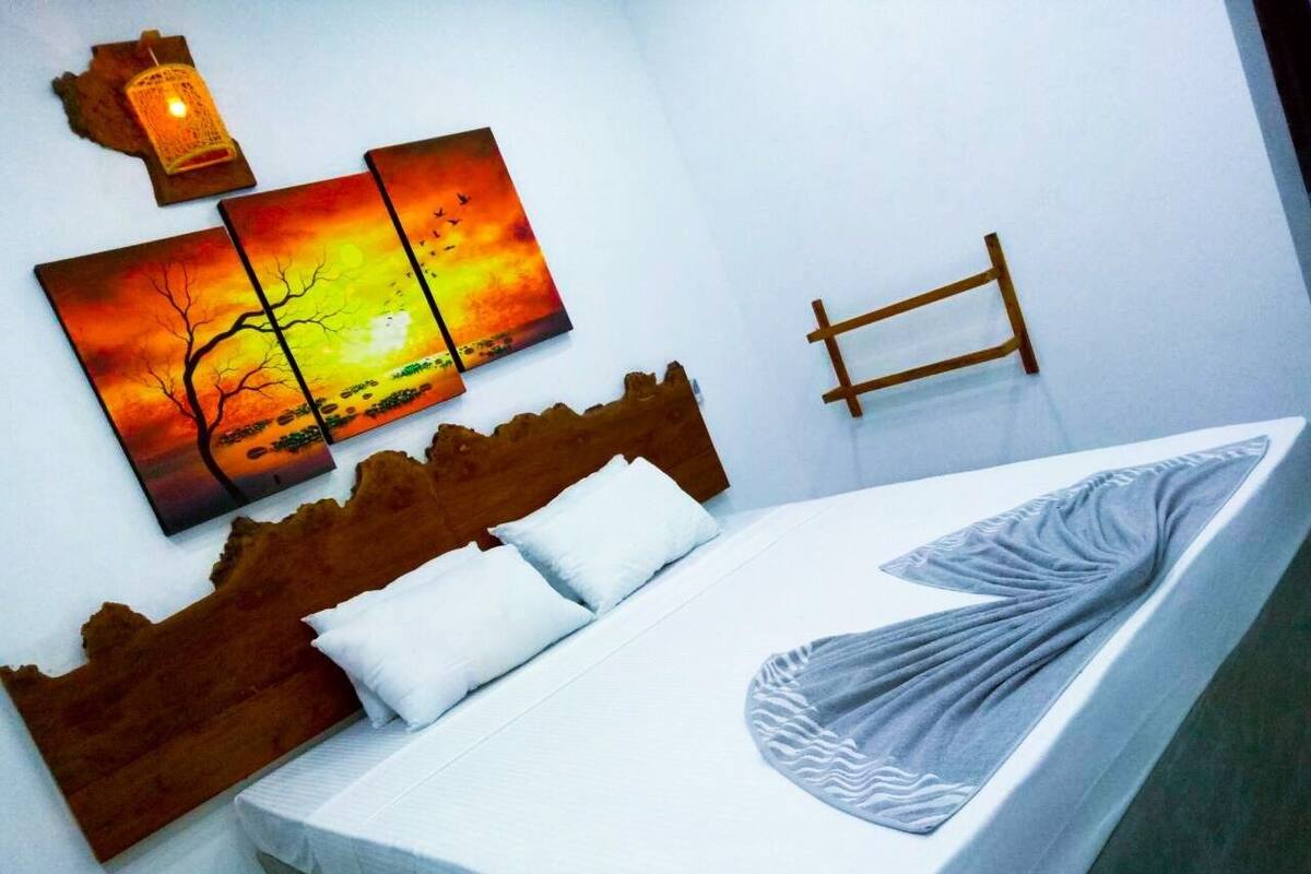 A bed with a white mattress and a grey blanket, a wooden headboard, and a wall-mounted wooden bed frame.