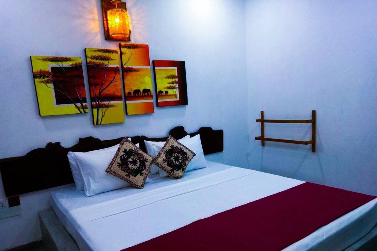 A bed with white bedding and a red throw, a nightstand with a lamp, and wall art depicting landscapes.