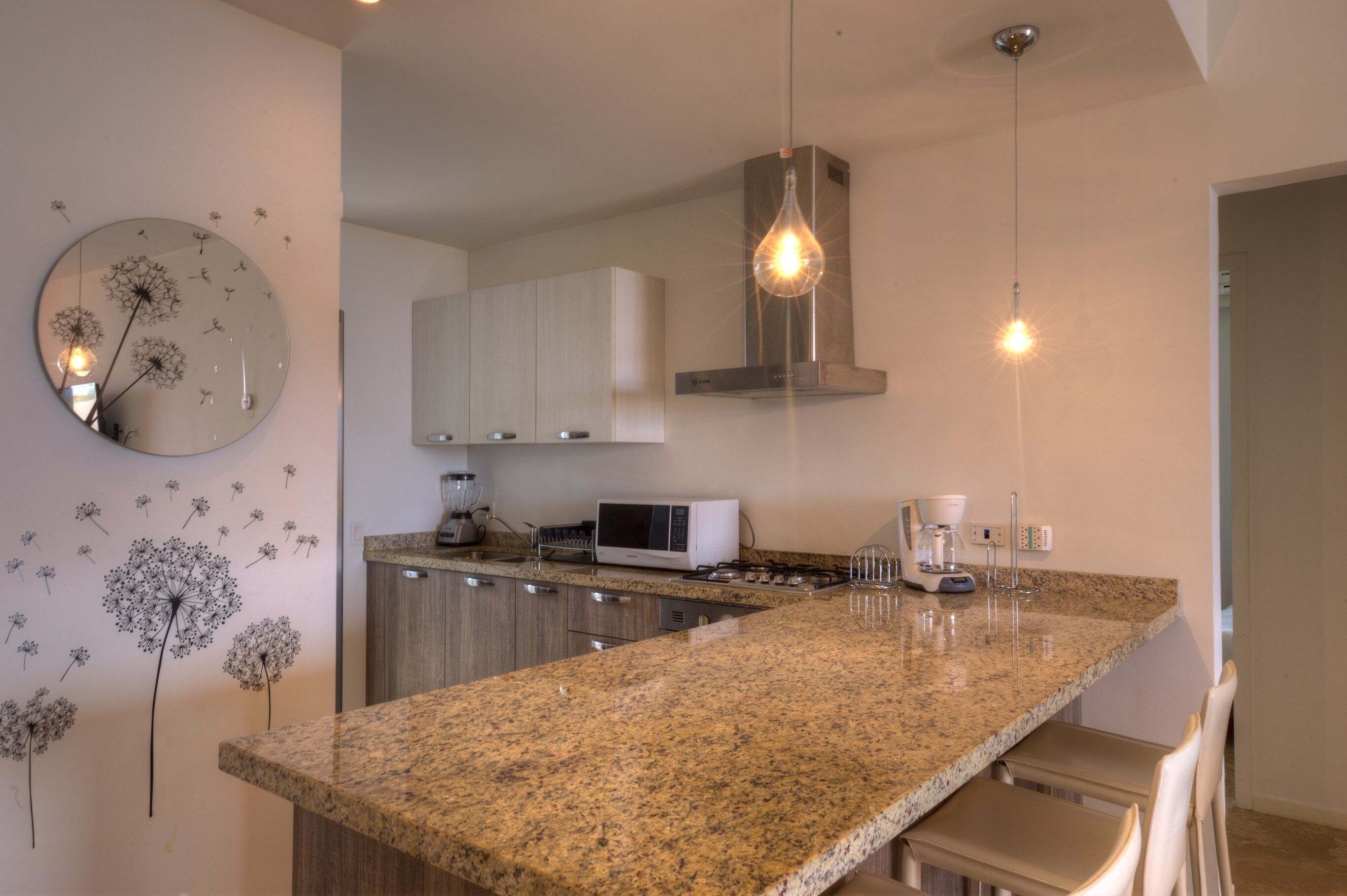 A modern kitchen with granite countertops, a microwave, a coffee maker, and a hanging light fixture.