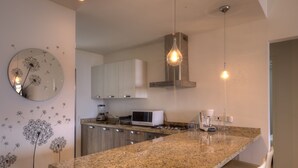 Una cocina moderna con encimeras de granito, microondas, cafetera y una lámpara colgante.