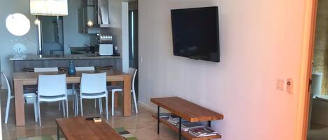 Ein modernes Wohnzimmer mit Essbereich, einer Küche im Hintergrund, einem Deckenventilator, einem Flachbildfernseher und einem gemusterten Teppich.