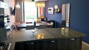 Una cocina moderna con encimera de granito, comedor con mesa y sillas, y sala de estar con sofá y televisor.