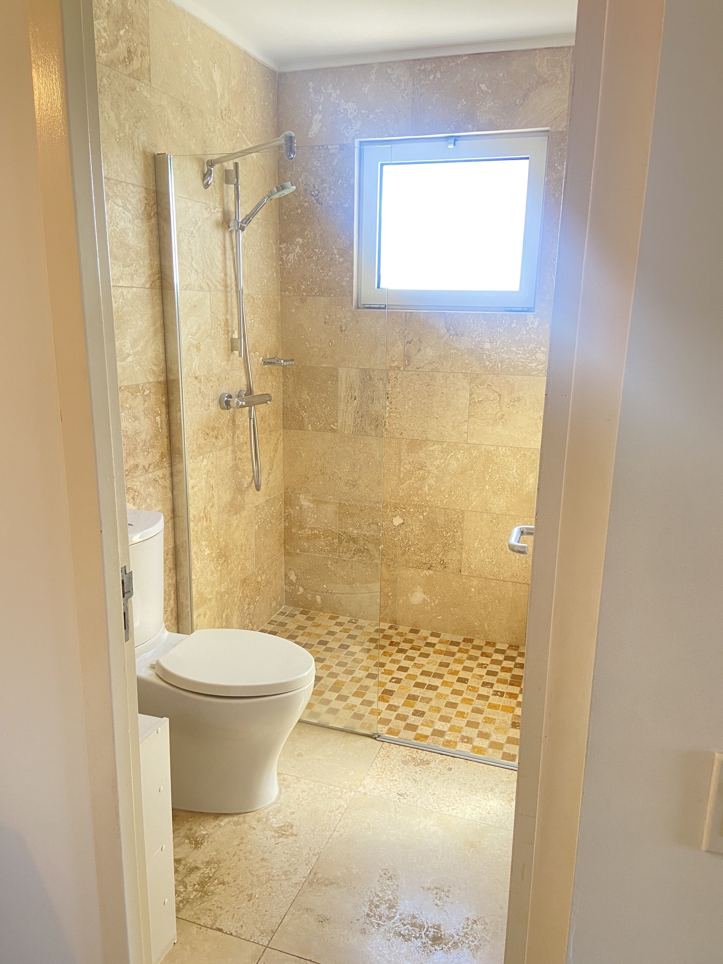 Une salle de bain avec une douche, des toilettes et une petite fenêtre.