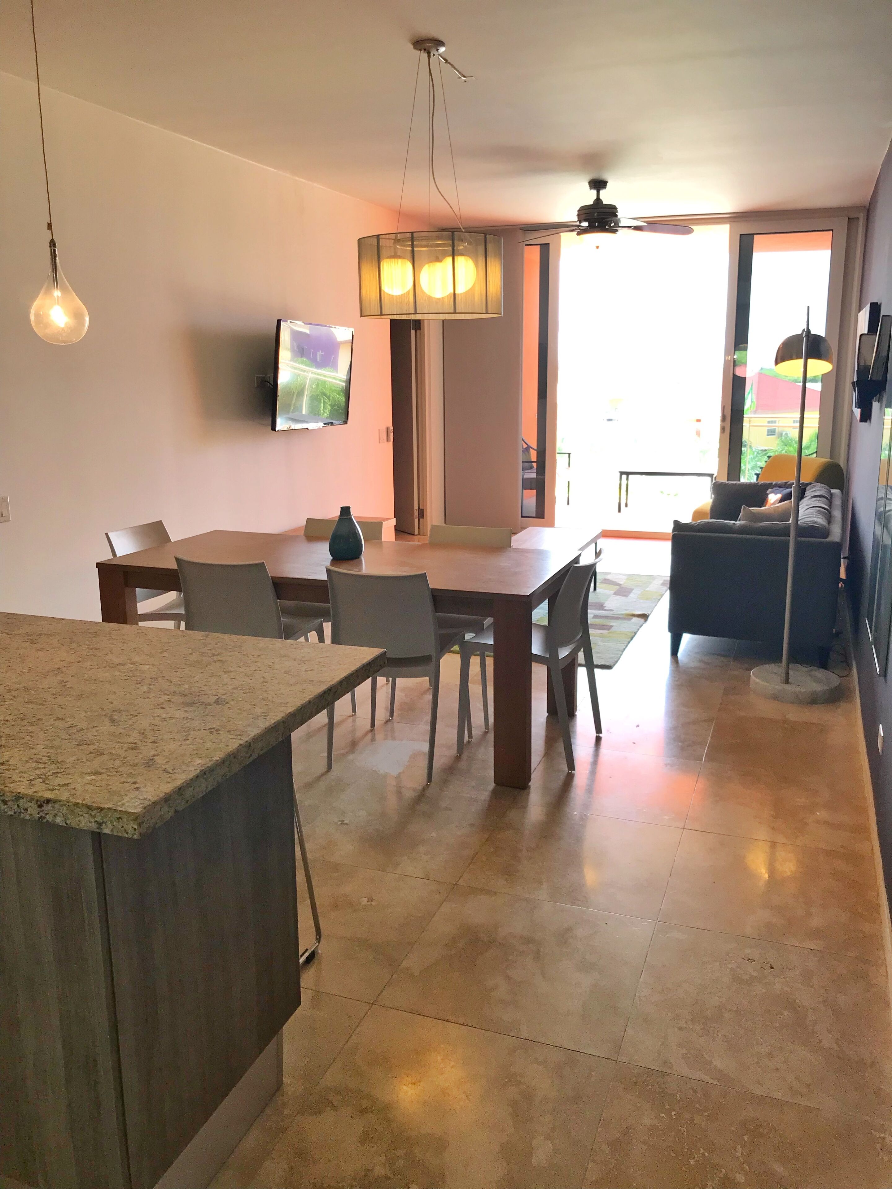 Eine moderne Küche mit Granitarbeitsplatten, eine Essecke mit Holztisch und -stühlen, ein an der Wand montierter Fernseher und ein Deckenventilator.