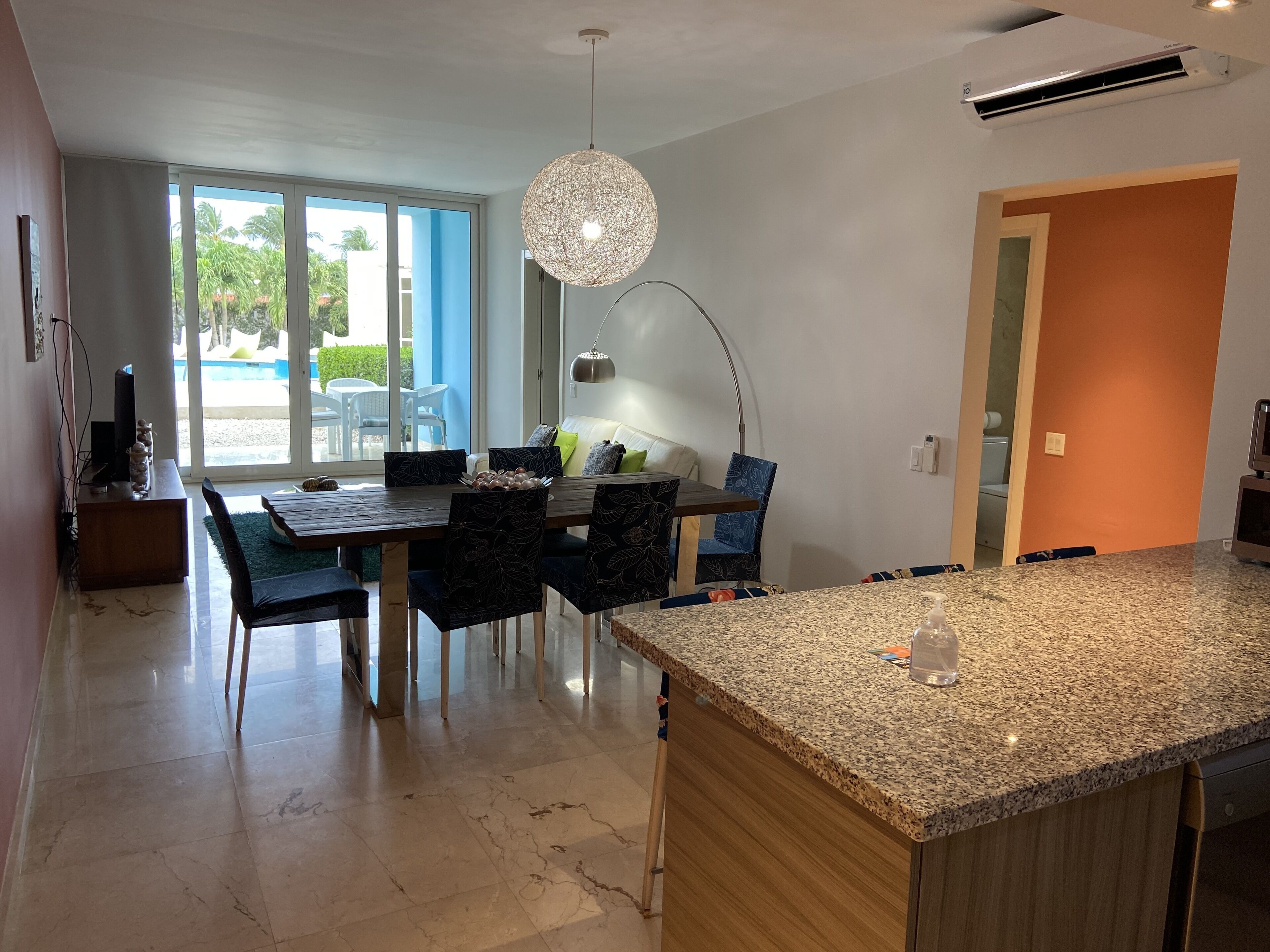 A modern kitchen with a granite countertop, a dining area with a table and chairs, and a large window with a view of palm trees.