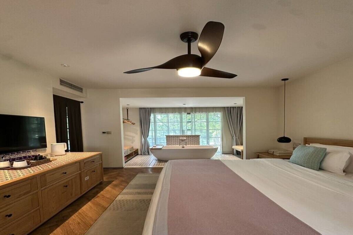 Quarto com cama, televisão, escrivaninha, banheira e ventoinha no teto.