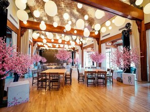 A spacious dining area with wooden tables and chairs, large windows, and decorative lighting.