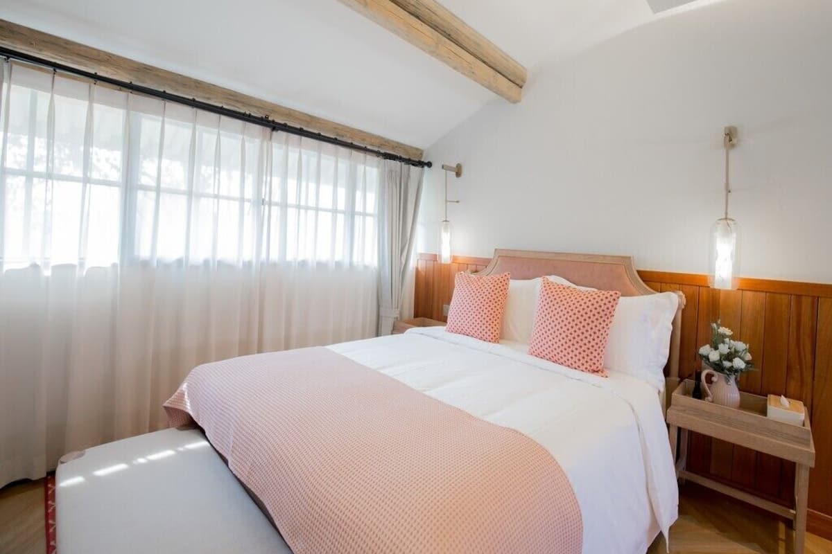 Quarto com cama, cabeceira de madeira, mesa de cabeceira e janela com cortinas.