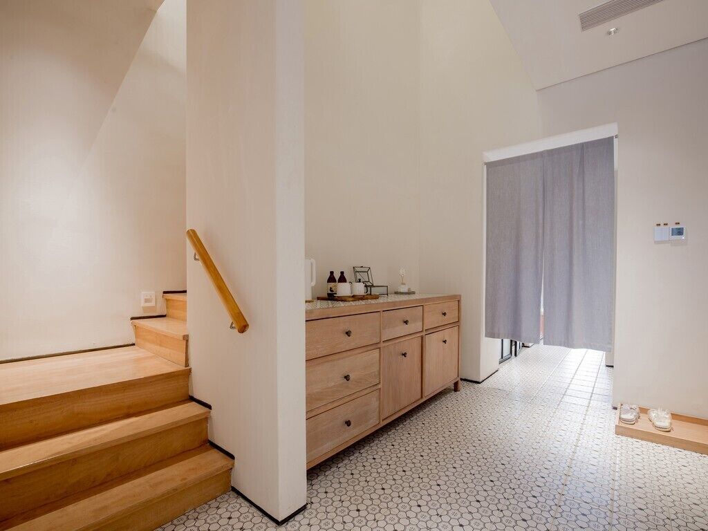 Un pasillo con escaleras de madera, un armario de madera y piso de baldosas.