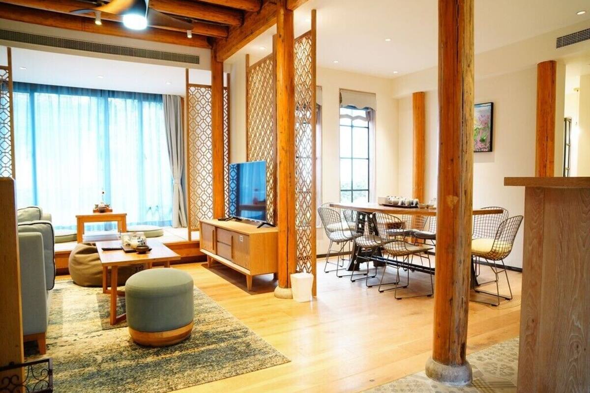 Uma sala de estar moderna com sofá, banqueta, televisão, mesa de jantar de madeira com cadeiras e um divisória decorativa.
