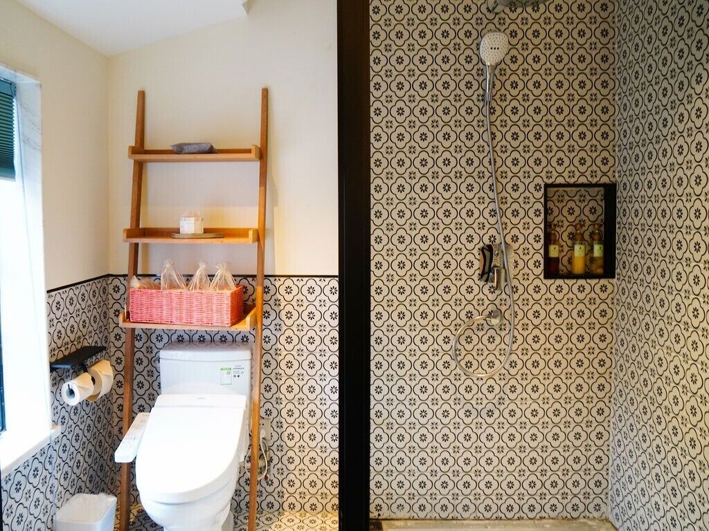Une salle de bain comprenant des toilettes, une étagère avec des articles de toilette et un espace douche équipé d’un pommeau de douche.