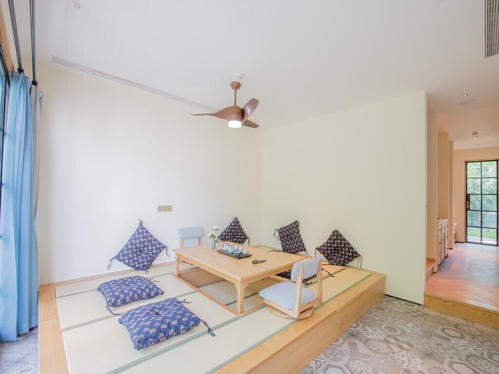 A room with tatami flooring, a low table, four chairs, and a ceiling fan.