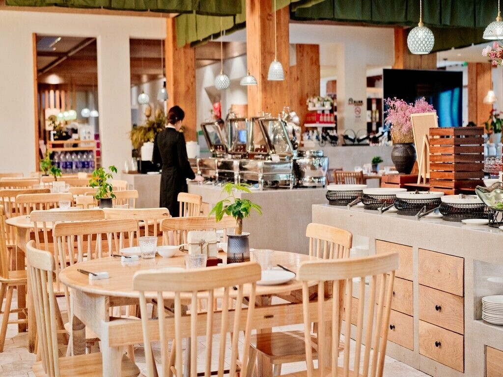 A restaurant with wooden tables and chairs, a bar area with stools, and a counter with coffee machines.