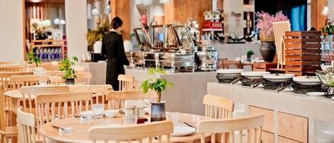 A restaurant with wooden tables and chairs, a bar area with stools, and a counter with coffee machines.