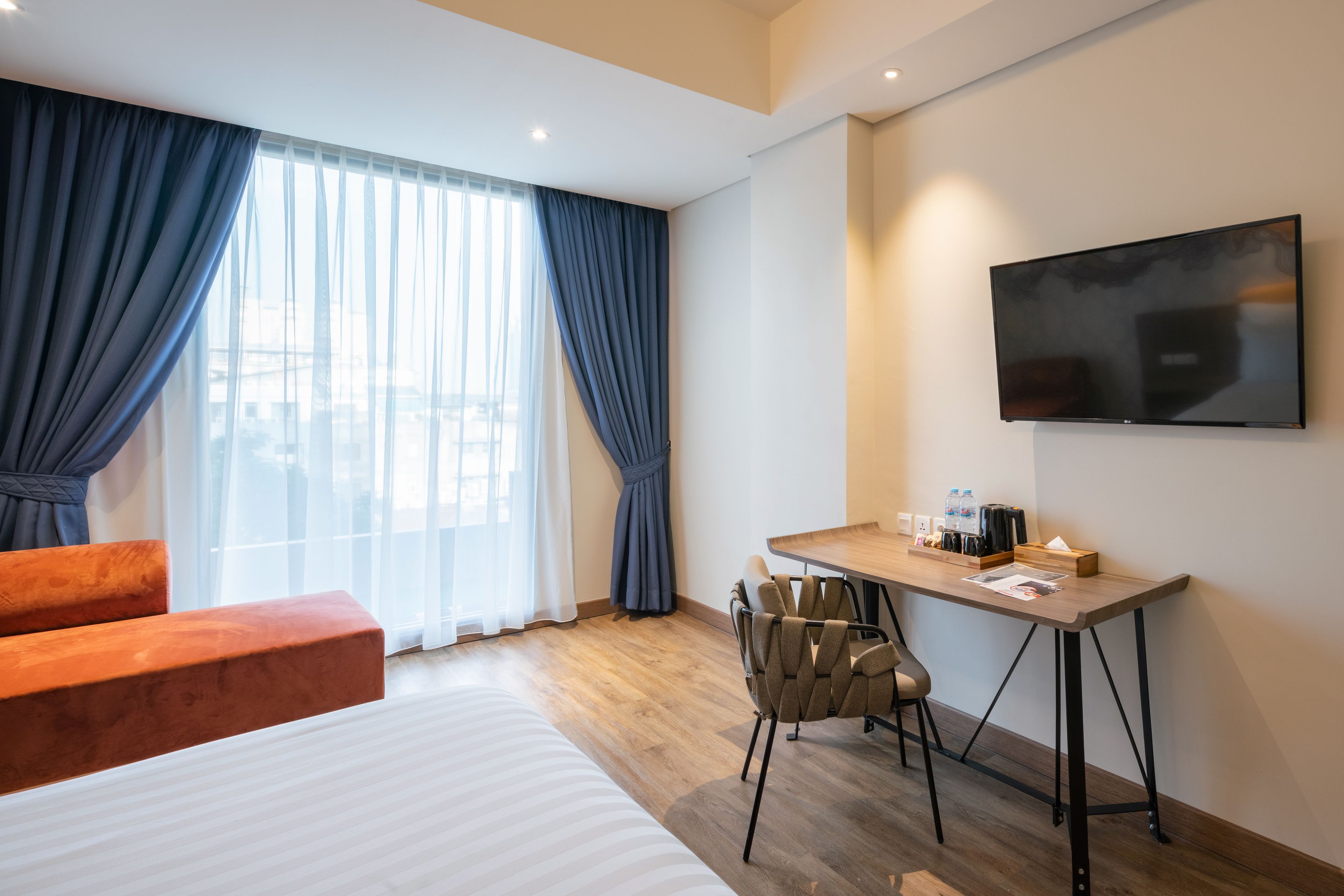 A hotel room with a bed, a desk with chairs, a TV, and a window with curtains.