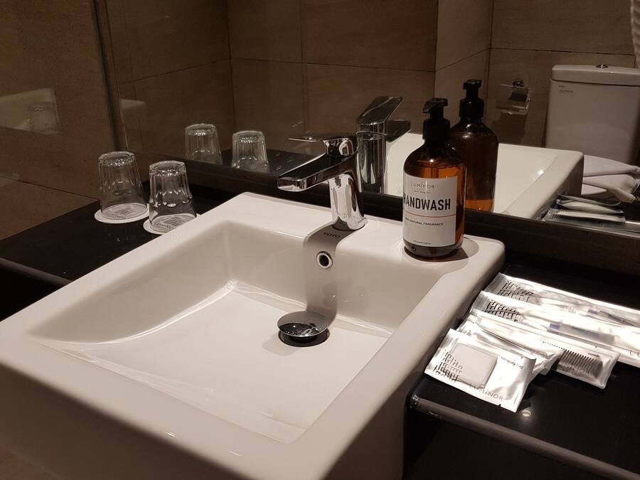 A bathroom sink with a mirror, a bottle of handwash, and a dental kit on the counter.