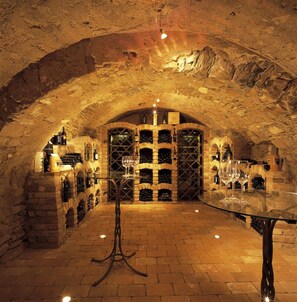 An underground wine cellar with stone arches, wine racks, and a glass table. - Hotel & Restaurant DAS RÖSSL (Windischgarsten)