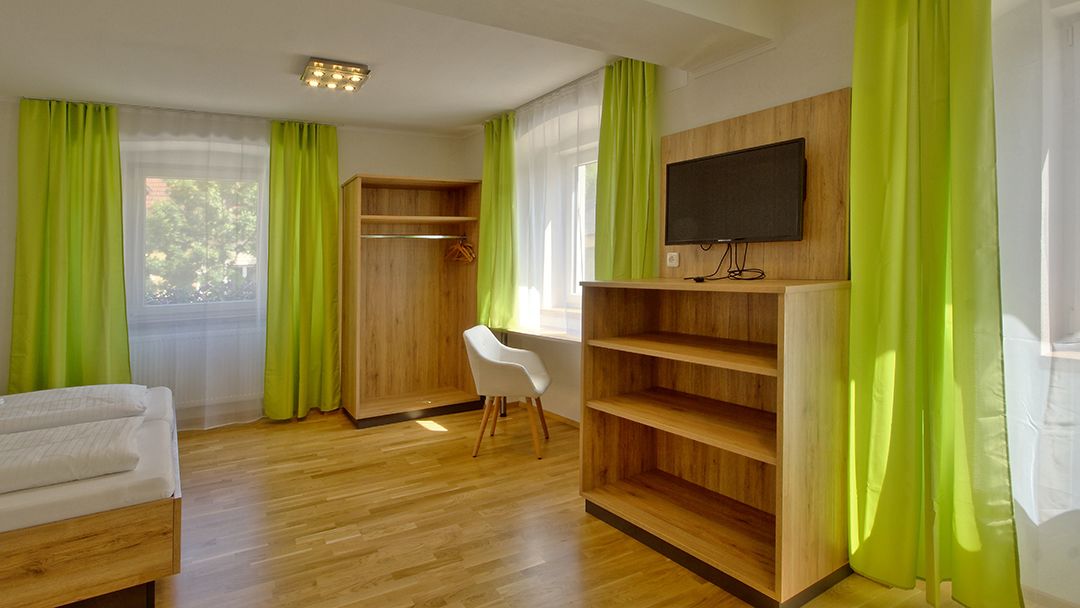 A room with a bed, a desk, a chair, a TV, and a wardrobe.