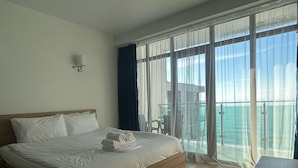 Ein Hotelzimmer mit einem großen Bett, einem Nachttisch und Meerblick durch große Fenster.