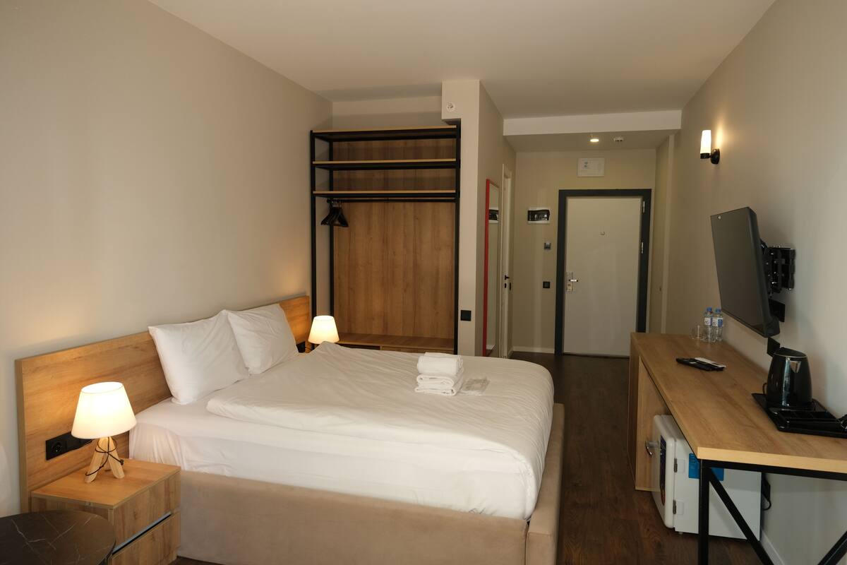 Ett hotellrum med en säng, sänglampor, ett skrivbord med en dator och en tv.