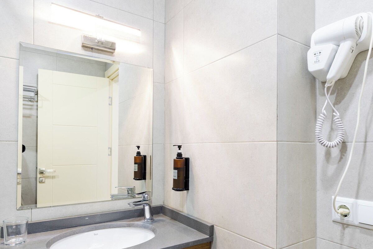 Een moderne badkamer met een grote spiegel, een wastafel en een aan de muur bevestigde haardroger.