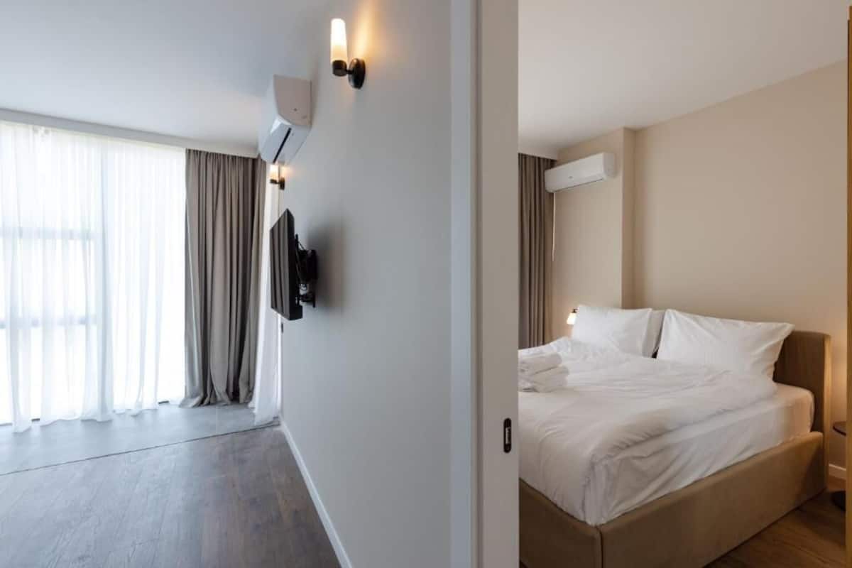 Ett modernt hotellrum med en stor säng, en tv som är monterad på väggen och ett fönster med gardiner.