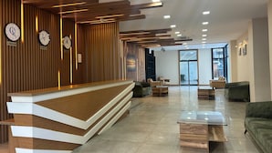 Ein moderner Empfangsbereich mit einem Holzbüro, Uhren, die die Zeit von London, Tokio und Chicago anzeigen, und einer geräumigen Sitzecke mit Sofas und einem Couchtisch.