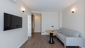 Ein modernes Wohnzimmer mit einem Flachbildfernseher, einem runden Tisch und einem grauen Sofa.