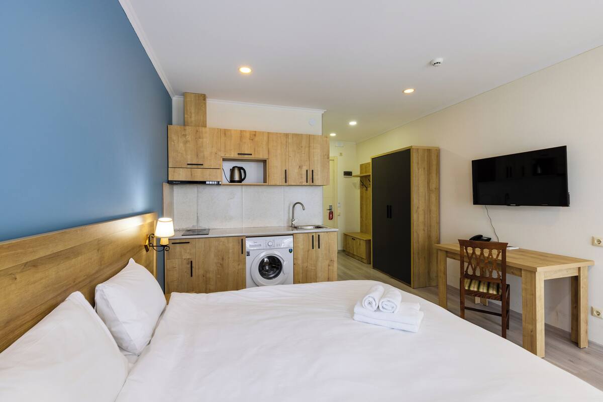 Ett hotellrum med en säng, en tvättmaskin, ett matbord och en tv.