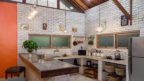 A kitchen with white brick walls, wooden beams, and a large island with stools. There are hanging lights, a chalkboard, and various kitchen appliances. - Luxury Enclosed Villa CHARM in Seminyak - 3 min walk to the beach (Seminyak)
