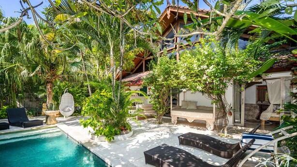 A pool area with lounge chairs, a small table, and a hanging chair surrounded by lush greenery and a building with a tiled roof. - Luxury Enclosed Villa CHARM in Seminyak - 3 min walk to the beach (Seminyak)