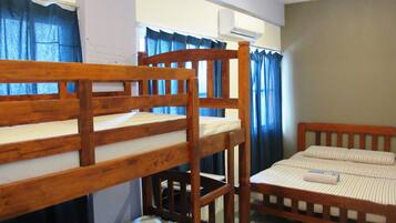 Dormitorio con literas, cabecero de madera, cama individual con colchón a rayas y ventana con cortinas azules.