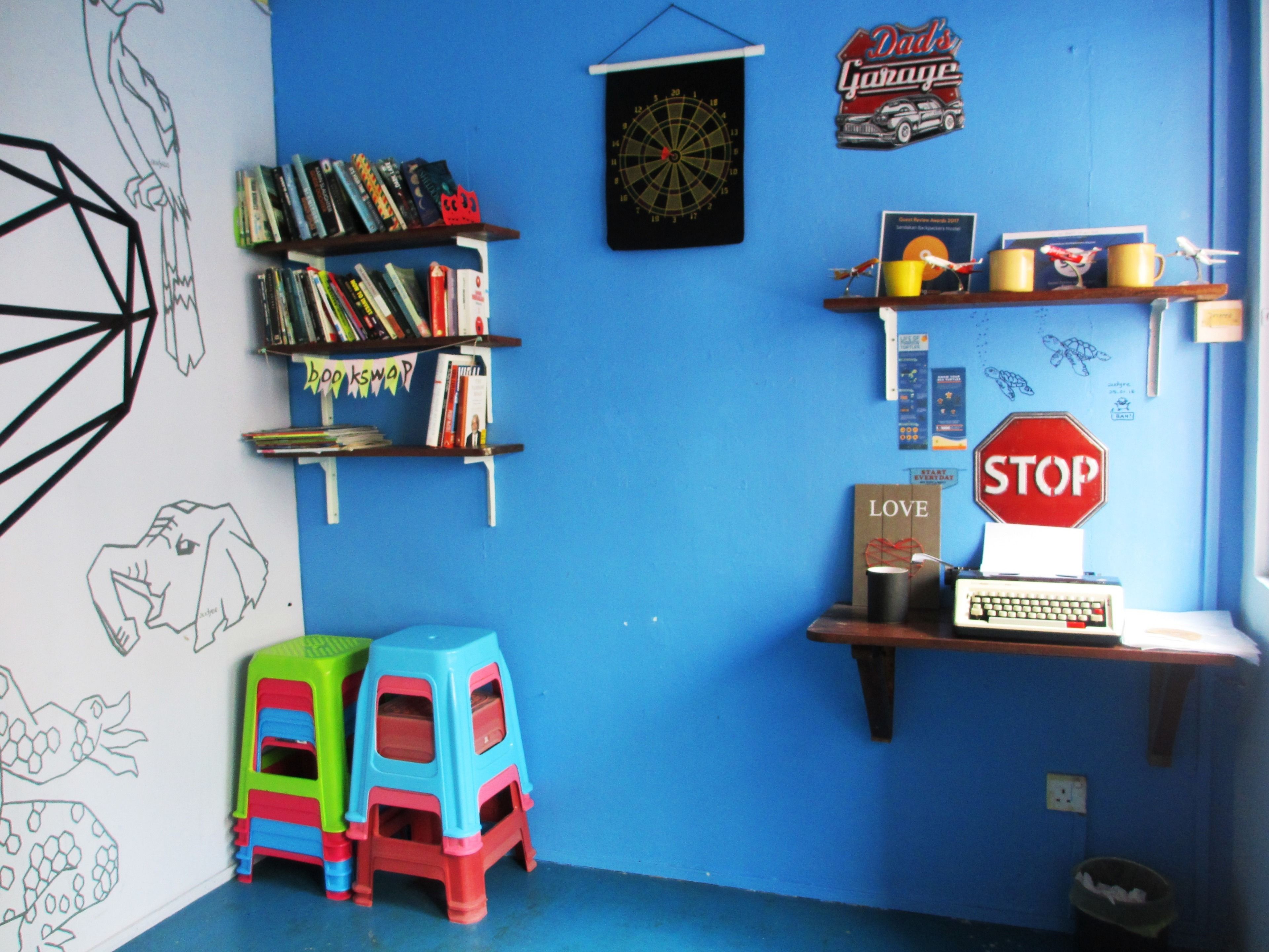 Ein Zimmer mit blauer Wand, einem Bücherregal, einer Dartscheibe, einem Stoppschild und einem Schreibtisch mit Computer.