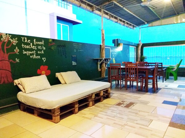A cozy room with a wooden pallet sofa, a dining table with chairs, and a green wall with a motivational quote.