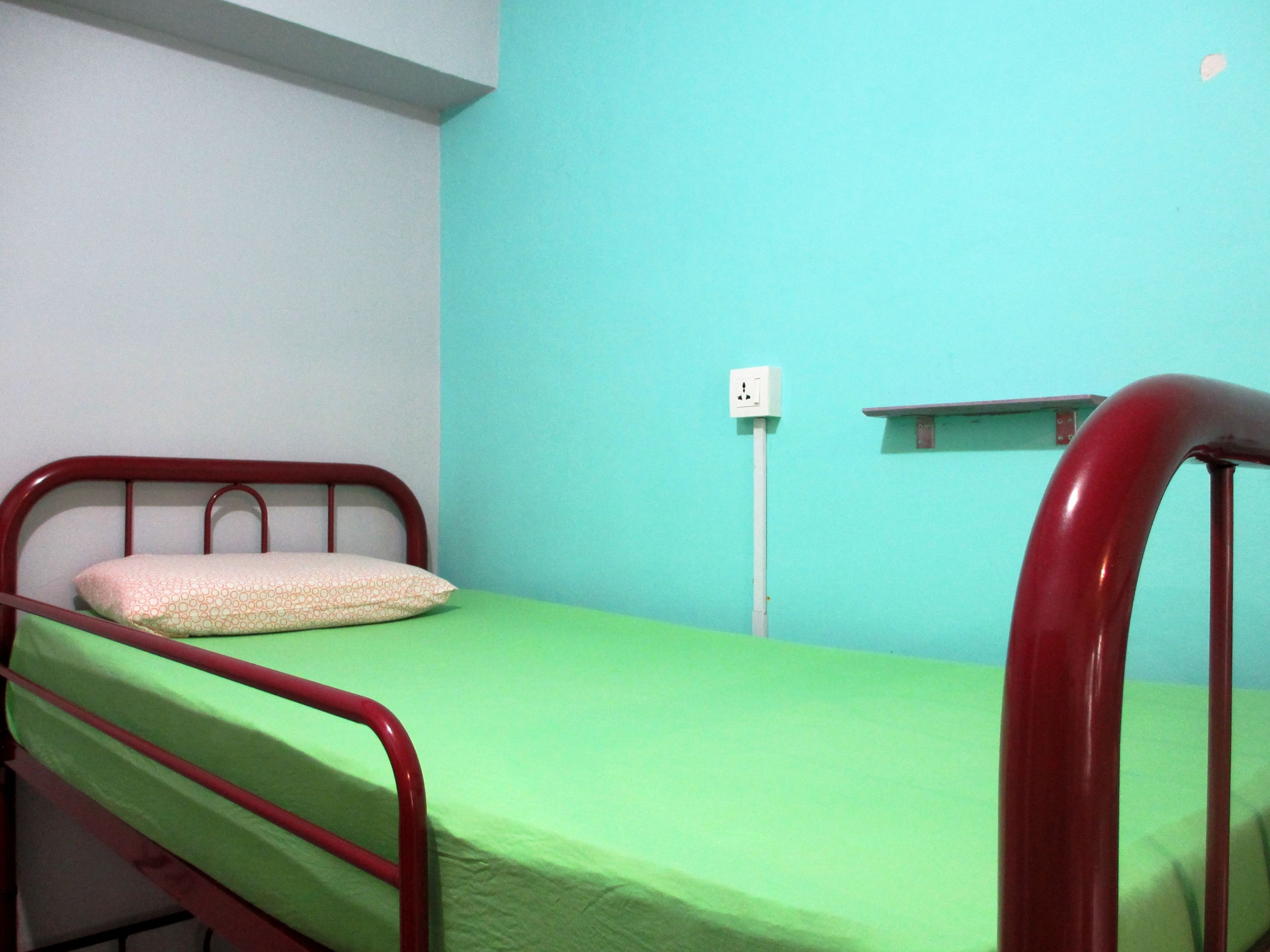 A single bed with a green mattress and a white pillow in a room with teal walls.