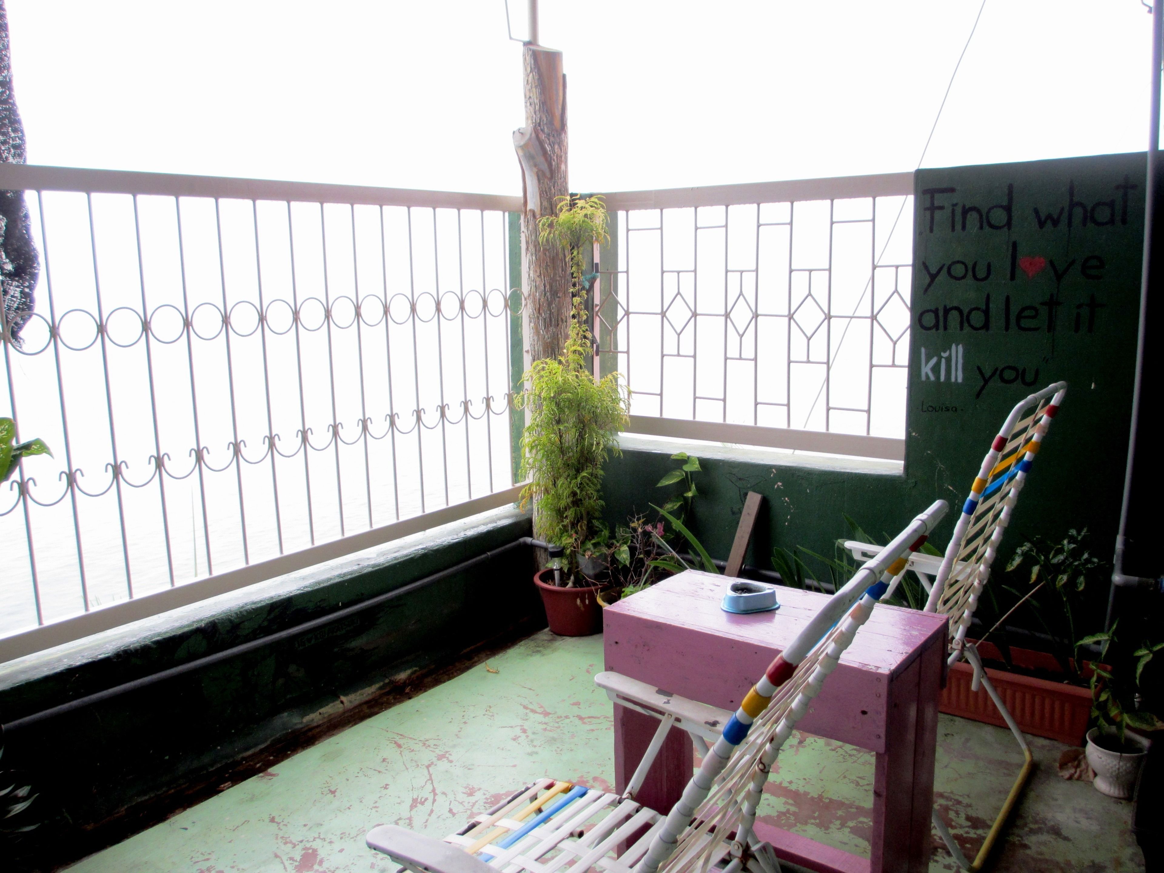 A balcony with a metal railing, a wooden chair, a small table, and potted plants.