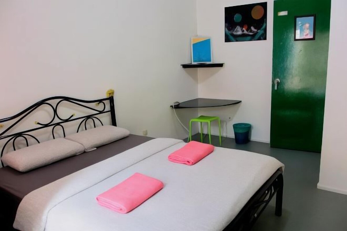 Un lit simple avec un cadre en métal, une porte verte et un petit tabouret.
