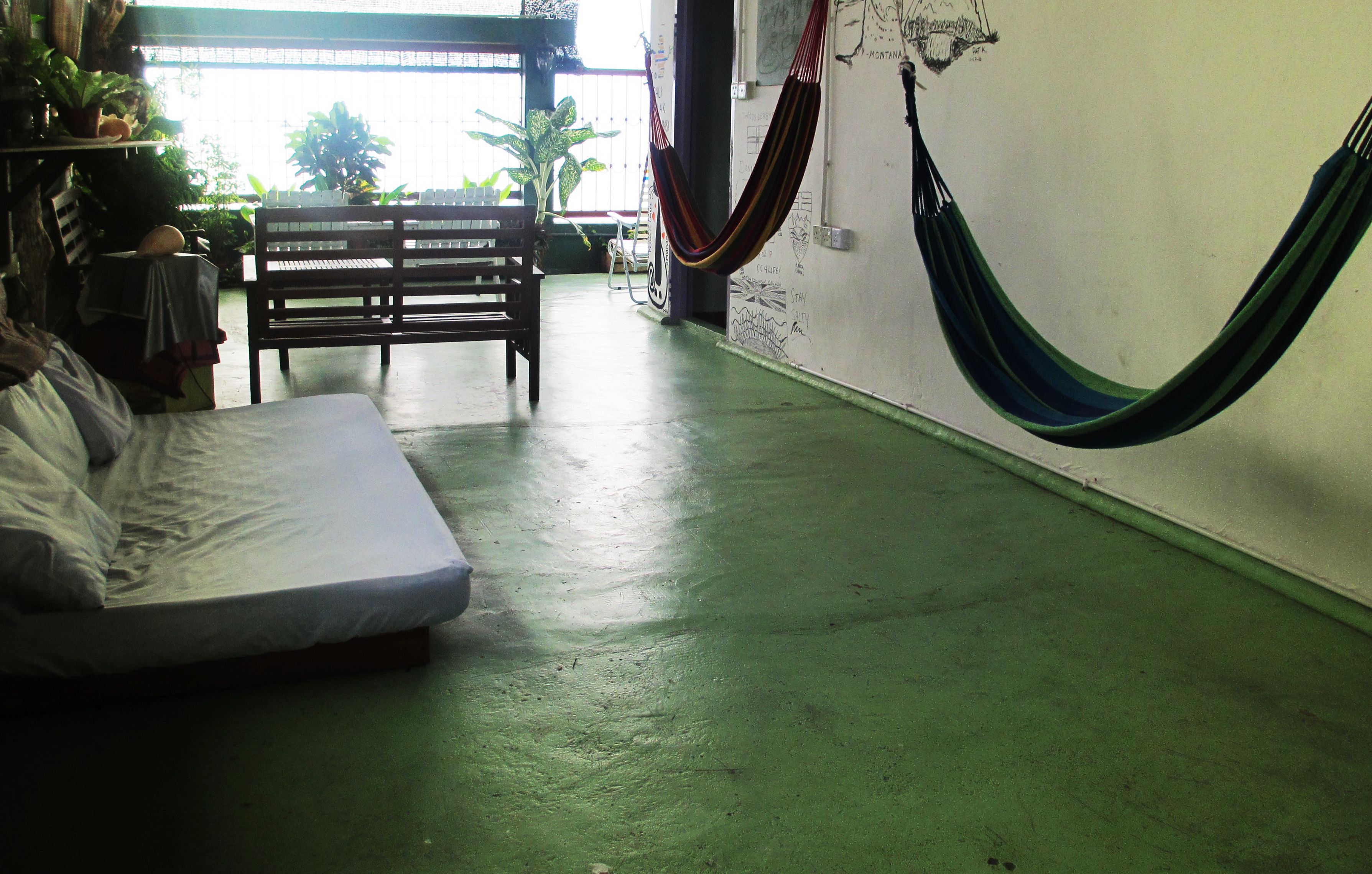 Quarto com cama, um banco, uma rede e plantas em vasos.