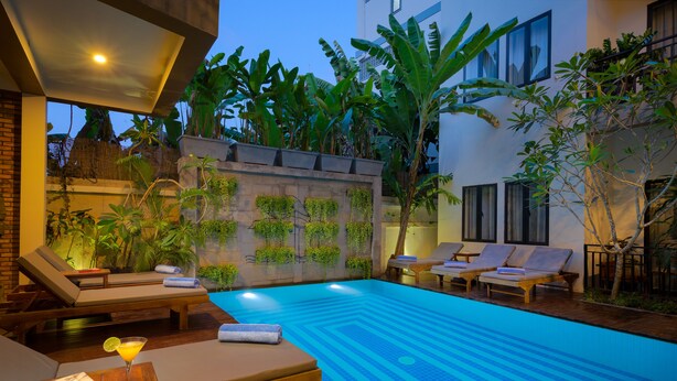 A swimming pool with lounge chairs and a bar area, surrounded by tropical plants and a stone wall. - Silver Smith Residence (Siem Reap)