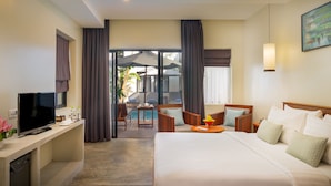 A hotel room with a bed, a desk with a TV, a dining area with a table and chairs, and a view of an outdoor pool area. - Silver Smith Residence (Siem Reap)