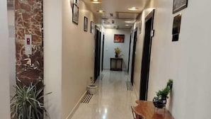 A hallway with marble flooring, a wooden console table, potted plants, and framed artwork on the walls. - Hotel Ozas Grand (Varanasi)