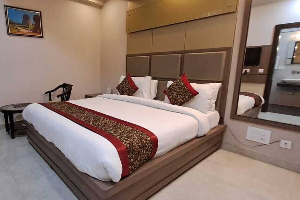 Ein Hotelzimmer mit einem großen Bett, einem Nachttisch, zwei Stühlen, einem kleinen Tisch, einem Bild an der Wand und einem großen Spiegel.