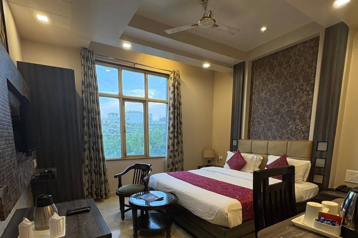 Ein Hotelzimmer mit einem Bett, einem Schreibtisch, einem Sessel, einem kleinen Tisch, einem Fernseher und einem Fenster mit Vorhängen.
